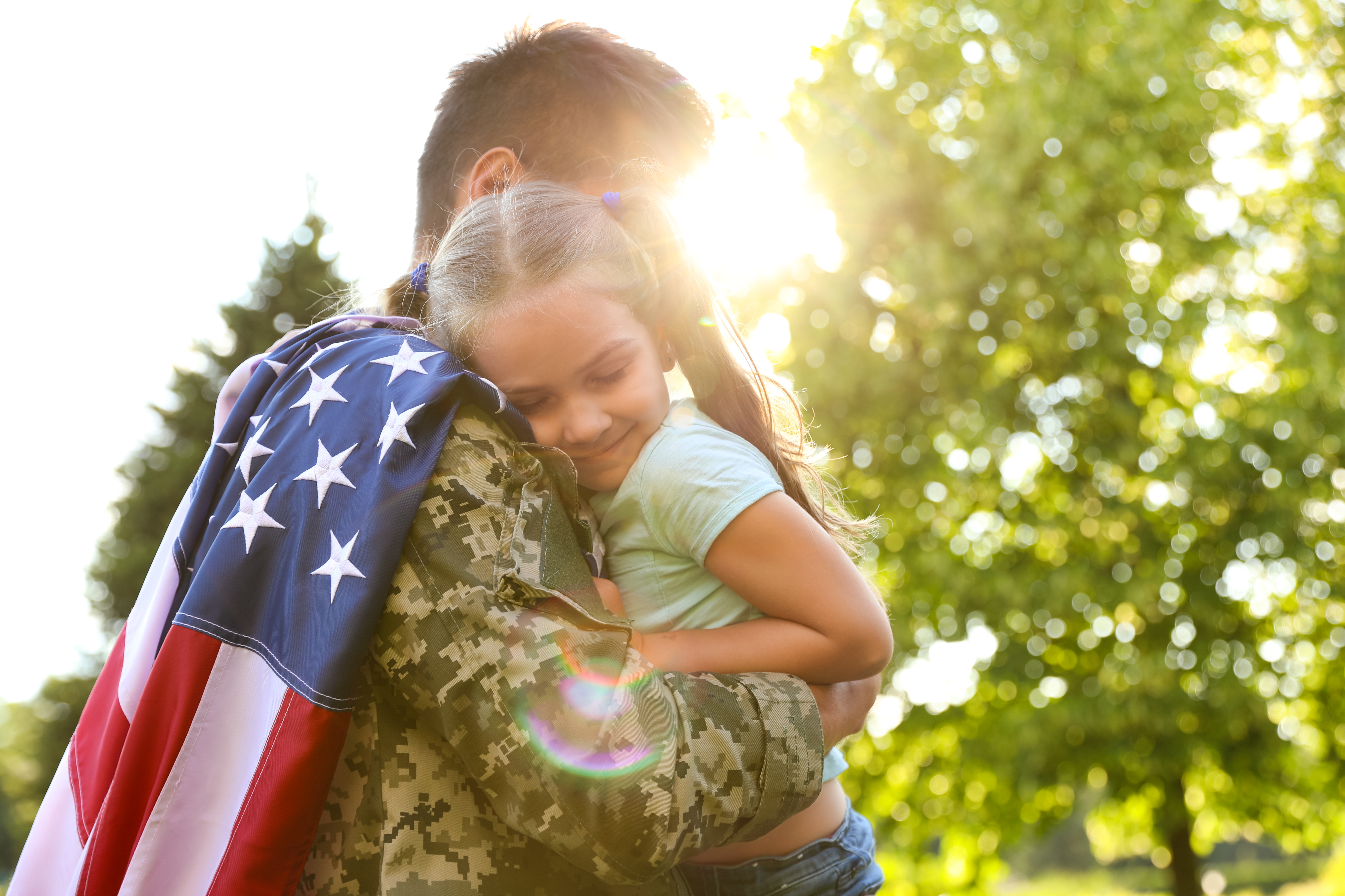 Military father hugging his daughter holding an American flag